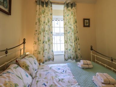 A bedroom with a metal bed frame floral bedding and curtains towels on the bed at Tizzie Whizie Cottage in Windermere