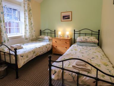 A bedroom with two single beds a wooden chest of drawers and a window at Tizzie Whizie Cottage in Windermere