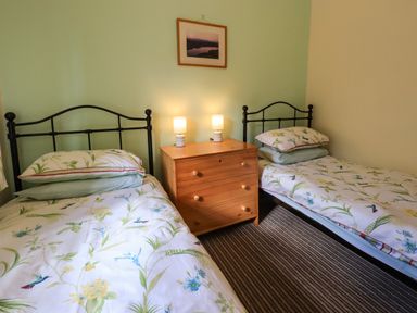 A bedroom with two single beds with floral bedding a wooden dresser with two lamps and a framed picture on the wall at Tizzie Whizie Cottage in Windermere
