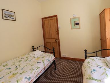 A bedroom with two single beds a wooden door a wardrobe and framed pictures on the walls at Tizzie Whizie Cottage in Windermere