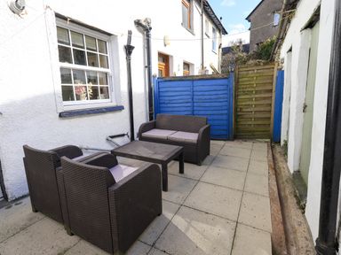 An outdoor patio area with brown wicker furniture including two armchairs a loveseat and a table against white walls at Tizzie Whizie Cottage in Windermere