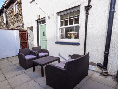 An outdoor patio with wicker furniture and a green door at Tizzie Whizie Cottage in Windermere