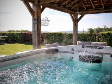 An outdoor hot tub with water flowing under a wooden gazebo with a lawn and hedge in the background at Hawkrigg Farm in Hawkshead