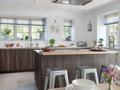 A kitchen with wooden island, metal stools, sink, countertop with fruit bowls and plants at Hawkrigg Farm in Hawkshead