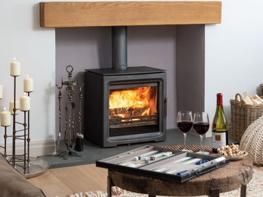 A wood burning stove with fire inside a room with candles on a stand and a table with a backgammon set and two glasses of red wine at Hawkrigg Farm in Hawkshead