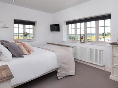 A bedroom with a bed with multiple pillows a wall-mounted TV and windows showing an outdoor view at Hawkrigg Farm in Hawkshead