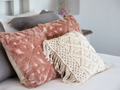 Decorative pillows including pink textured and white macrame on a bed at Hawkrigg Farm in Hawkshead