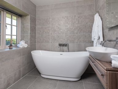 A bathroom with a freestanding bathtub a sink on a wooden vanity a window with rolled towels and a bathrobe hanging at Hawkrigg Farm in Hawkshead