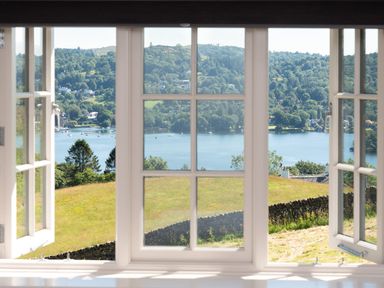 A view of a lake with boats and hills through an open white window at Hawkrigg Farm in Hawkshead