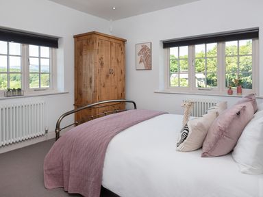 A bedroom with a bed covered by a quilt and pillows next to wooden wardrobe and two windows with black blinds at Hawkrigg Farm in Hawkshead