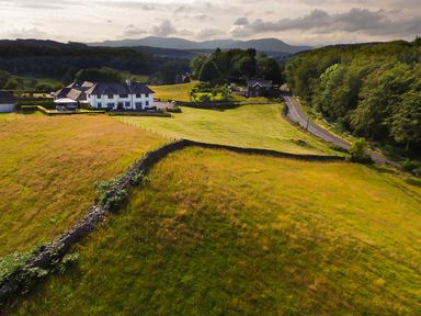 A rural landscape with fields and stone walls a few houses and a road among trees at Hawkrigg Farm Hawkshead