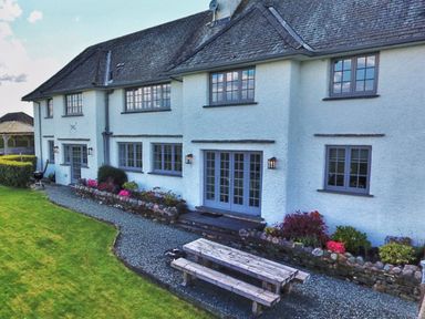 A backyard with a gravel path a wooden picnic table a flower bed and a barbecue grill outside a two-story house at Hawkrigg Farm in Hawkshead