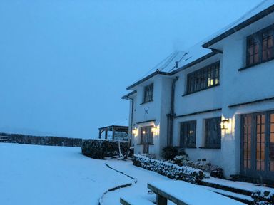 A snowy yard with a white house and lit exterior lights at Hawkrigg Farm in Hawkshead