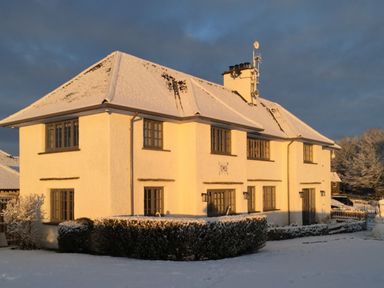 A two-story house with snow on the roof and ground with hedges in front at Hawkrigg Farm in Hawkshead