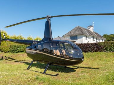 A black helicopter parked on grass with a house and hedge in the background at Hawkrigg Farm in Hawkshead