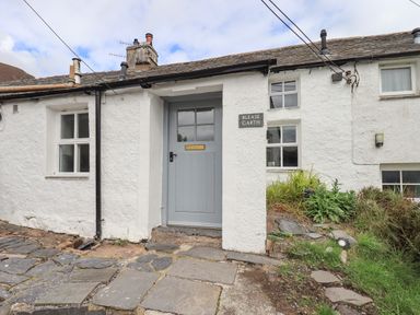The front door of a white stone house with a slate roof and stone pathway at Blease Garth in Threlkeld