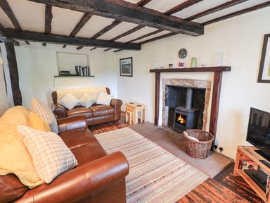 A living room with leather sofas a rug a wood burning stove and wooden beams on the ceiling at Blease Garth in Threlkeld