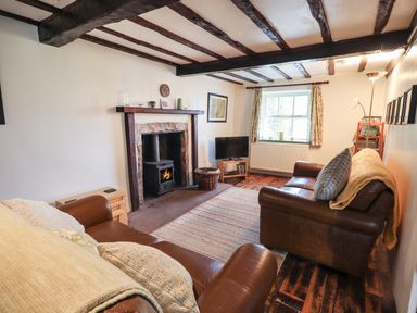 A living room with wooden beams on ceiling a fireplace with wood burner two leather sofas a television and a window at Blease Garth in Threlkeld