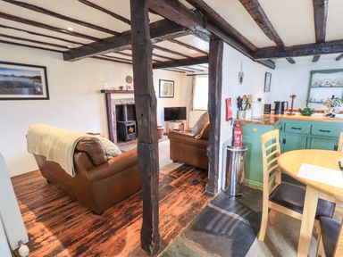 An open plan living room and kitchen with exposed wooden beams and leather sofas at Blease Garth in Threlkeld