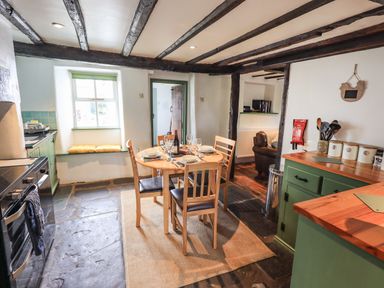 A kitchen with a wooden dining table and chairs stone flooring and exposed wooden beams at Blease Garth in Threlkeld