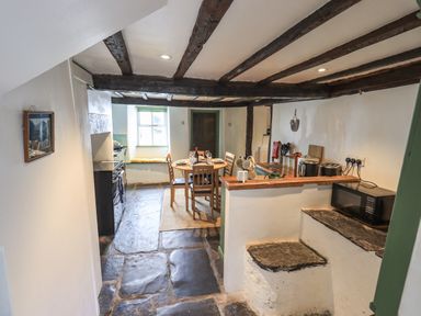 A kitchen dining area with wooden beams stone floor and a round dining table at Blease Garth in Threlkeld