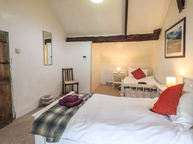 A bedroom with two beds red pillows bedside tables lamps a chair and a wall picture at Blease Garth in Threlkeld