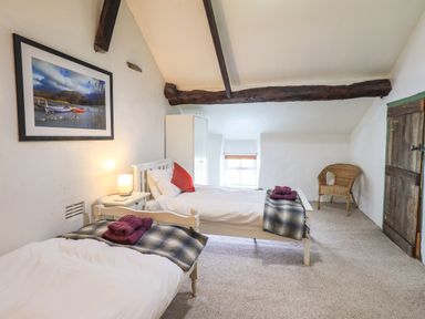 A bedroom with two single beds a wooden wardrobe a wicker chair and a framed picture on the wall at Blease Garth in Threlkeld
