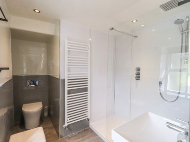 A bathroom with a toilet, shower area, sink, radiator, and window at Blease Garth in Threlkeld