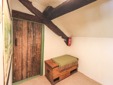A room with a wooden door a wooden chest with a green blanket and a fire extinguisher on a beam at Blease Garth in Threlkeld