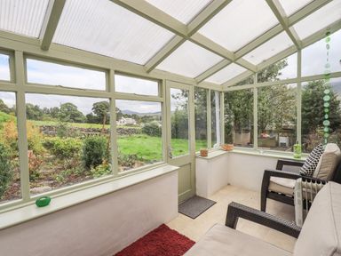 A conservatory with wicker chairs and a red rug overlooking a garden at Blease Garth in Threlkeld