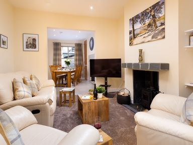 A living room with beige leather sofas a wooden coffee table and a television next to a fireplace at Dovedale in Keswick