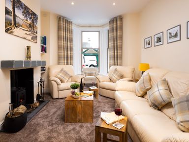 A living room with cream sofas wooden tables fireplace and bay window at Dovedale in Keswick