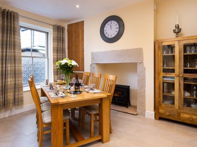 A dining room with wooden table and chairs set for dinner a clock above a fireplace and a wooden cabinet with glassware at Dovedale in Keswick
