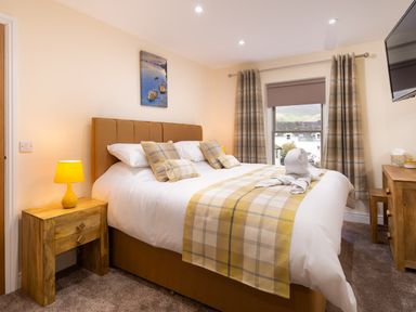 A bedroom with a bed with plaid pillows and blanket next to wooden furniture and a window at Dovedale in Keswick