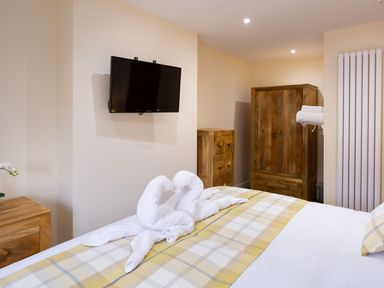 A bedroom with a mounted television wooden furniture and towel swans on the bed at Dovedale in Keswick