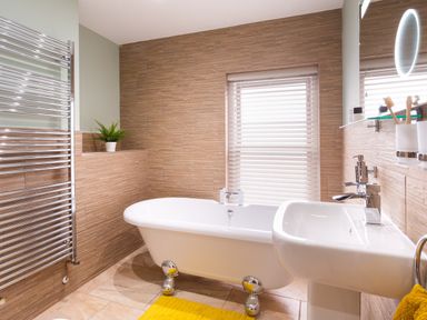 A bathroom with a freestanding bathtub a sink yellow rug and a plant at Dovedale in Keswick