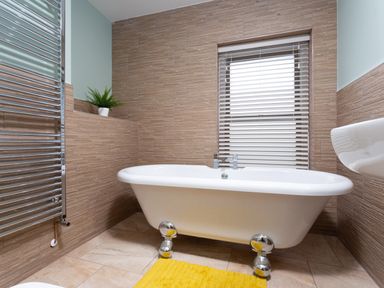 A bathroom with a white freestanding bathtub yellow rug and chrome towel radiator at Dovedale in Keswick