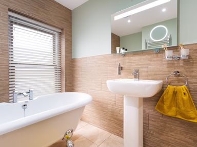 A bathroom with a bathtub a sink a mirror a yellow towel and a window with blinds at Dovedale in Keswick