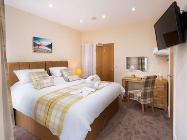 A bedroom with a large bed a desk with a chair a wall-mounted television and a door at Dovedale in Keswick