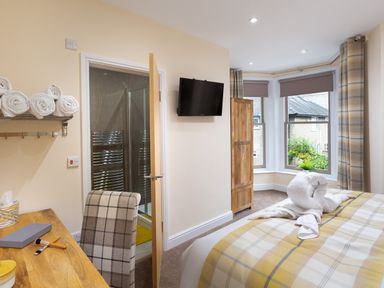 A bedroom with a bed covered in a plaid blanket and towel swans near a bay window at Dovedale in Keswick