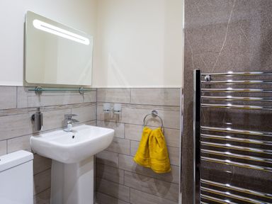 A bathroom with a white sink and mirror above it a yellow towel on a ring and a chrome towel radiator at Dovedale in Keswick