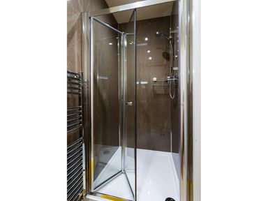 A shower area with glass doors a showerhead and a metal towel radiator at Dovedale in Keswick
