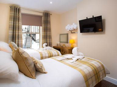 A bedroom with two single beds a window with plaid curtains a wall-mounted tv and a wooden desk at Dovedale in Keswick