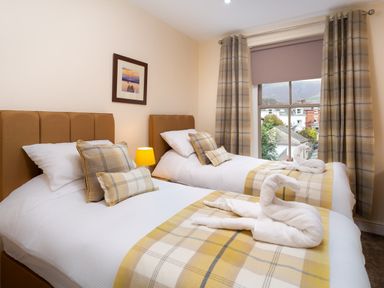 A bedroom with two single beds with plaid blankets and pillows and towel swans on the beds at Dovedale in Keswick