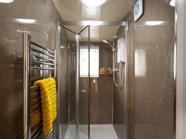 A shower enclosure with glass doors and a yellow towel on a heated towel rail at Dovedale in Keswick