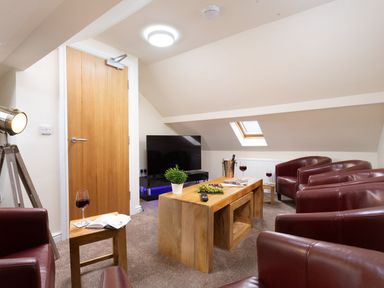 A living room with brown leather chairs a wooden coffee table with a plant and grapes a television and a wooden door at Dovedale in Keswick