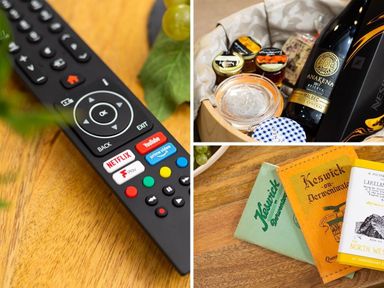 A remote control on a wooden surface a basket with jars and a bottle of wine and booklets on a wooden table at Dovedale in Keswick