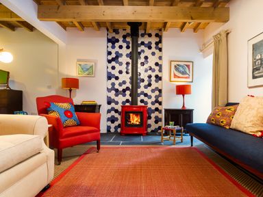 A living room with a red armchair a blue sofa and a red wood stove with hexagon tiles at Kentmere Hall Bank Barn in Kentmere