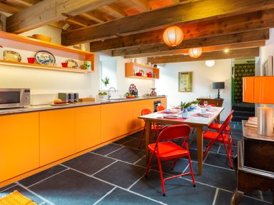A kitchen with orange cabinets and red chairs around a dining table at Kentmere Hall Bank Barn in Kentmere