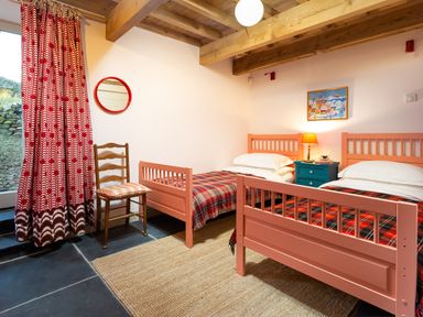 A bedroom with two single beds red plaid bedding a wooden chair with a cushion red patterned curtains and a bedside table with a lamp at Kentmere Hall Bank Barn in Kentmere